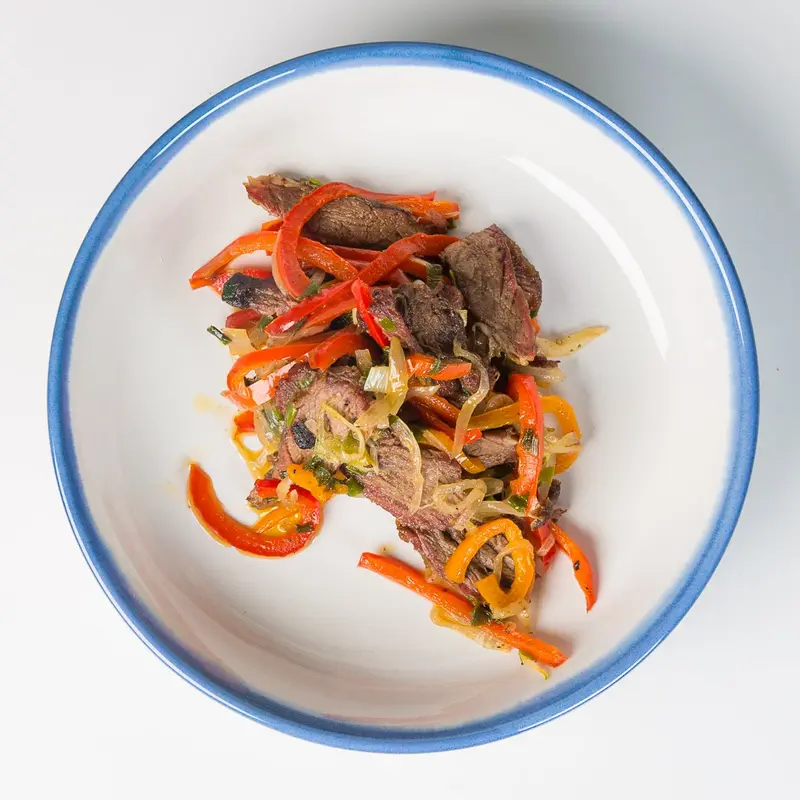 Suya-spiced grilled beef with charred red peppers and onions in a blue-rimmed bowl